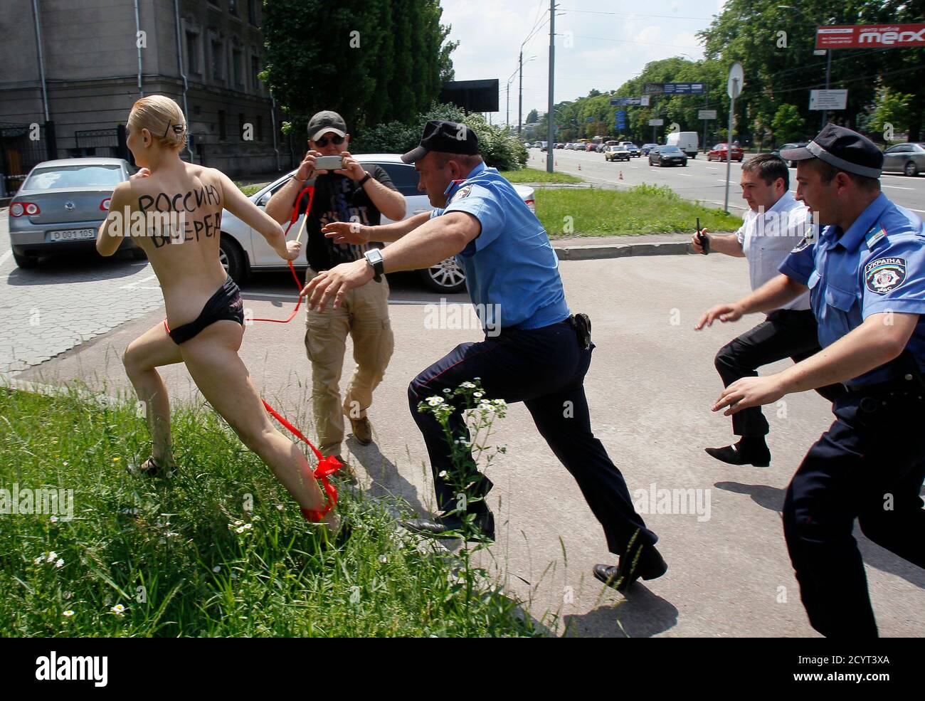 Interior Ministry officers and a security guard chase an activist from the women's rights group FEMEN, as she stages a demonstration outside the Russian embassy in response to Russian President Vladimir Putin's announcement of his separation from his wife Lyudmila, in Kiev, June 7, 2013. The woman intended to portray Olympic rhythmic gymnast Alina Kabayeva, referring to speculations that Putin could date the former sportswoman, according to FEMEN's press release. The words on the woman's back read, 'Push Russia forward!' REUTERS/Gleb Garanich (UKRAINE - Tags: CIVIL UNREST POLITICS) Stock Photo