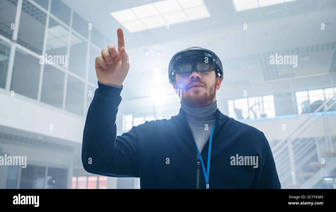 Automotive Engineer Using Augmented Reality Headset and Moving Virtual Pieces in the Air. In Innovation High Tech Laboratory Facility with Futuristic Stock Photo