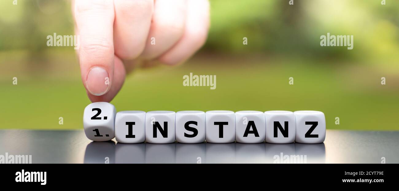 Hand turns dice and changes the German expression '1. Instanz' (first instance) to '2. Instanz' (second instance). Stock Photo