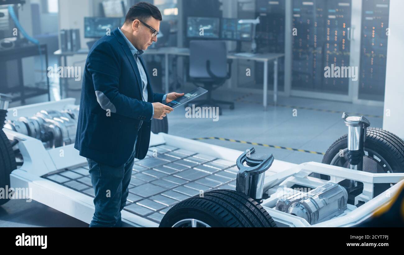 Automotive Design Engineer Looking at Technical Drawing of an Electric Car Chassis Prototype on a Tablet. In Innovation Laboratory Facility Concept Stock Photo