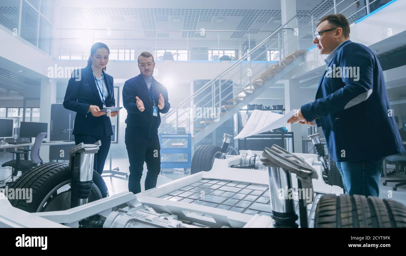 Automotive Design Engineers Talking while Working on Electric Car Chassis Prototype. In Innovation Laboratory Facility Concept Vehicle Frame Includes Stock Photo