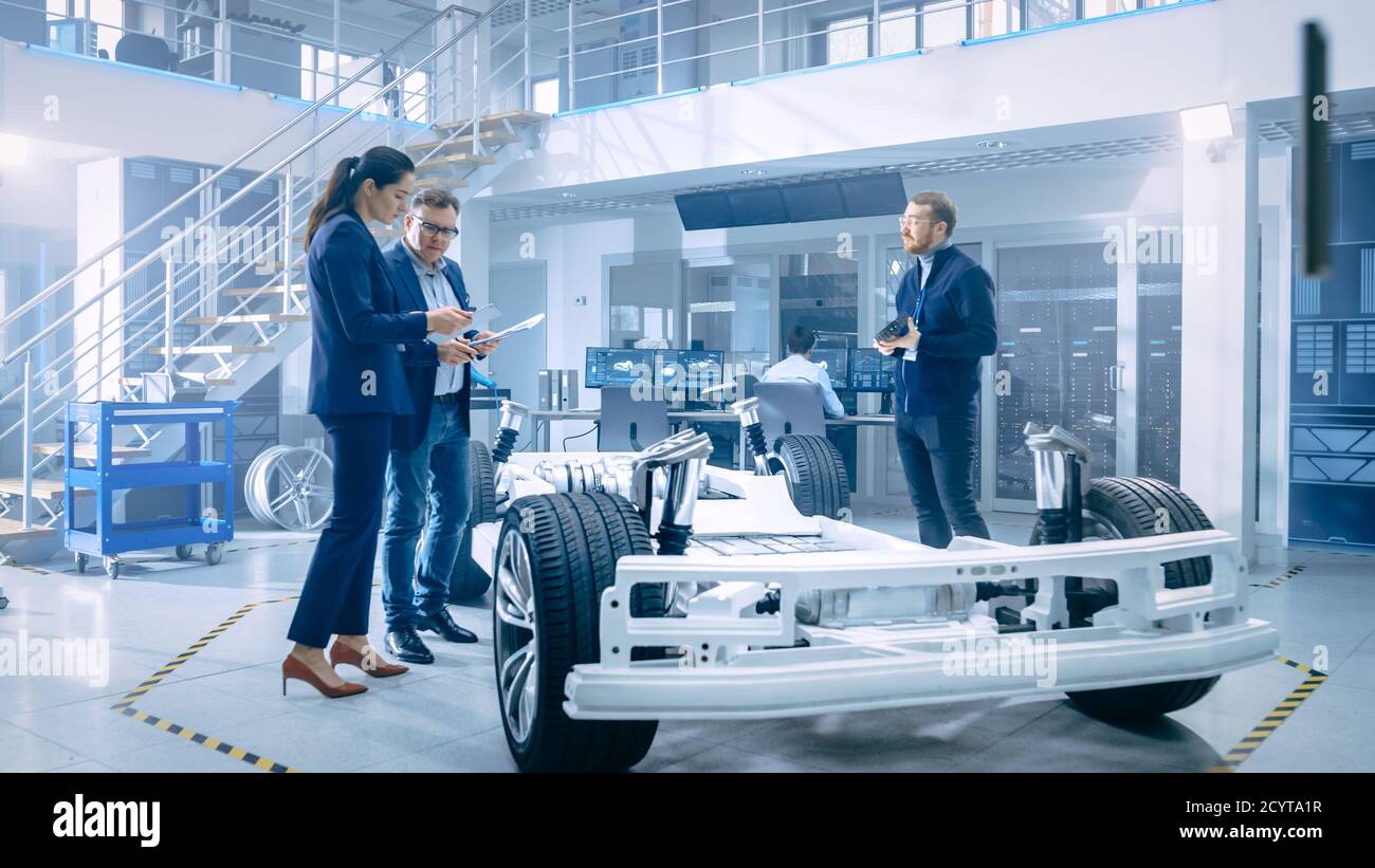 Automotive Design Engineers Talking while Working on Electric Car Chassis Prototype. In Innovation Laboratory Facility Concept Vehicle Frame Includes Stock Photo