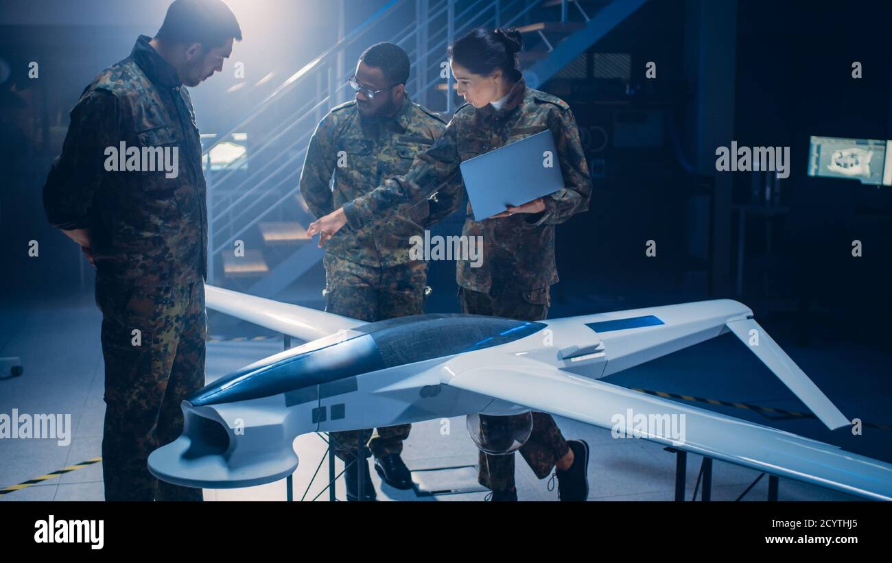 Army Aerospace Engineers Work On Unmanned Aerial Vehicle Drone. Uniformed Aviation Experts Talk, Using Laptop. Industrial Facility with Aircraft for Stock Photo