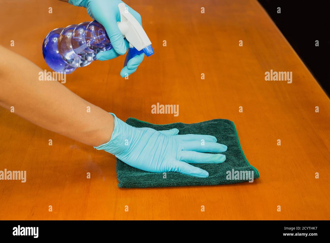 Hand with glove cleaning table with disinfectant bottle and towel COVID