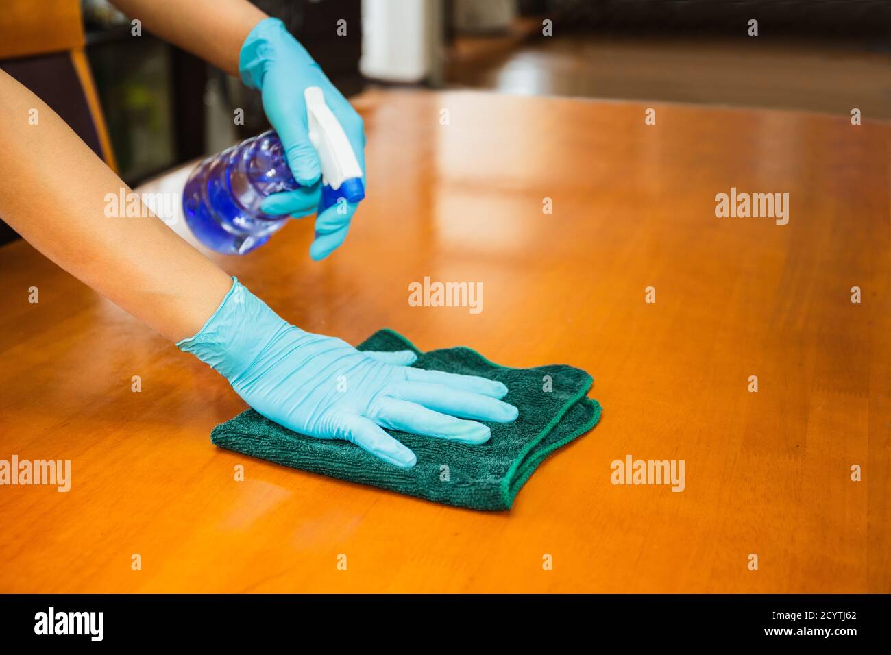 Hand with glove cleaning table with disinfectant bottle and towel COVID