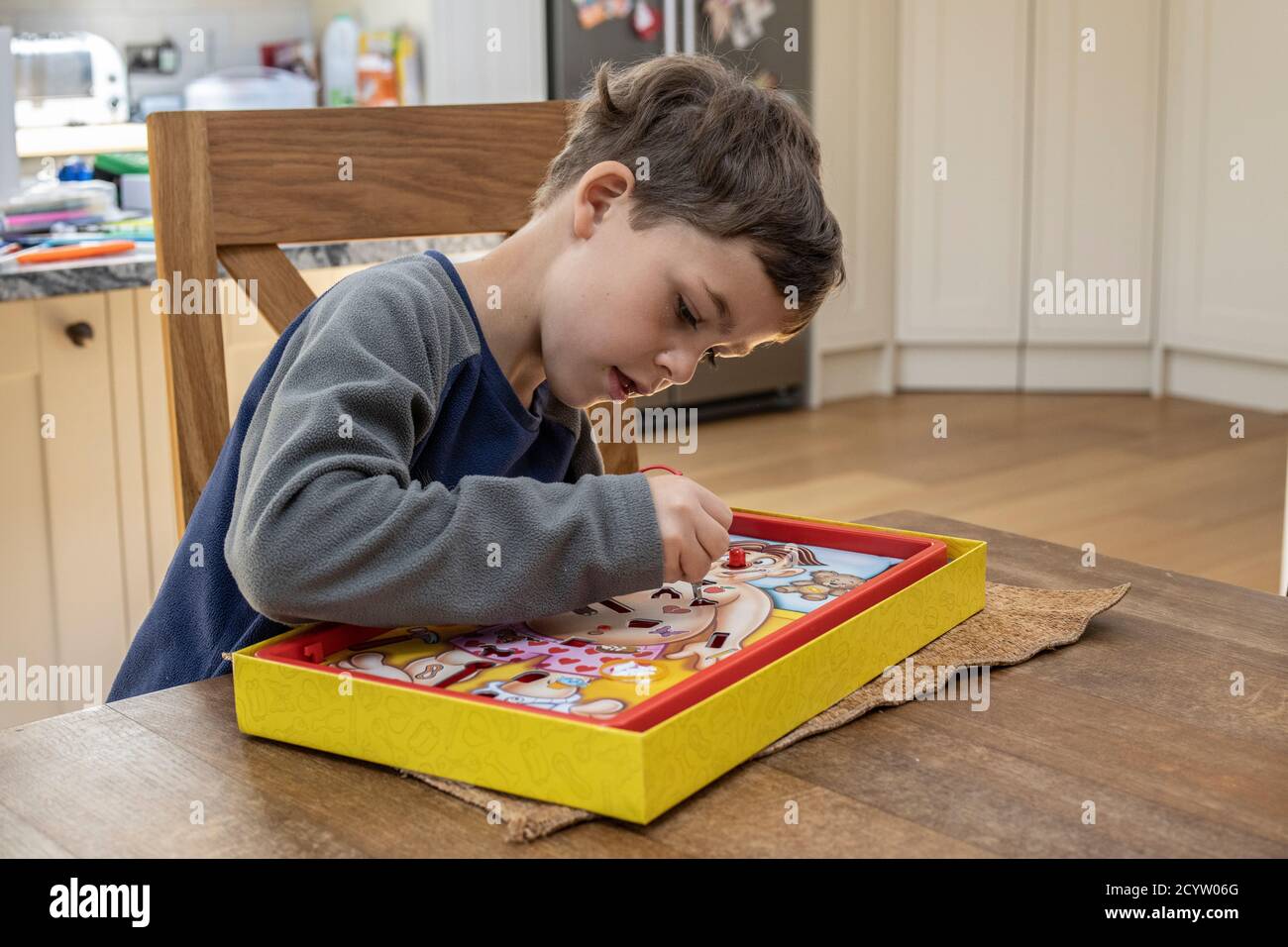 Boy playing classic game of 'Operation' challenges you to remove body parts using tweezers without setting off the buzzer, made by Hasbro games, UK Stock Photo