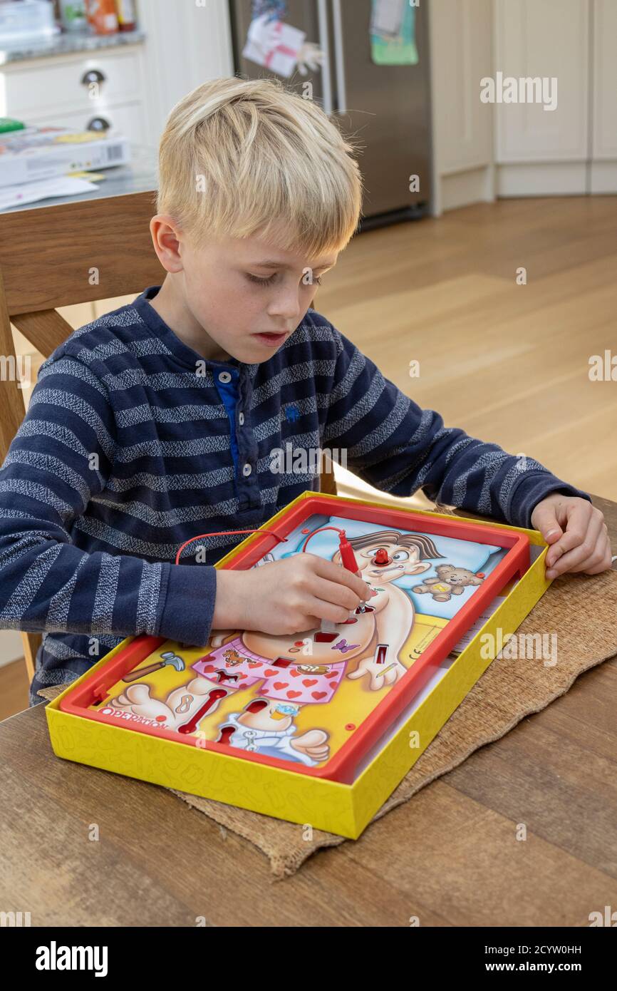 Boy playing classic game of 'Operation' challenges you to remove body parts using tweezers without setting off the buzzer, made by Hasbro games, UK Stock Photo