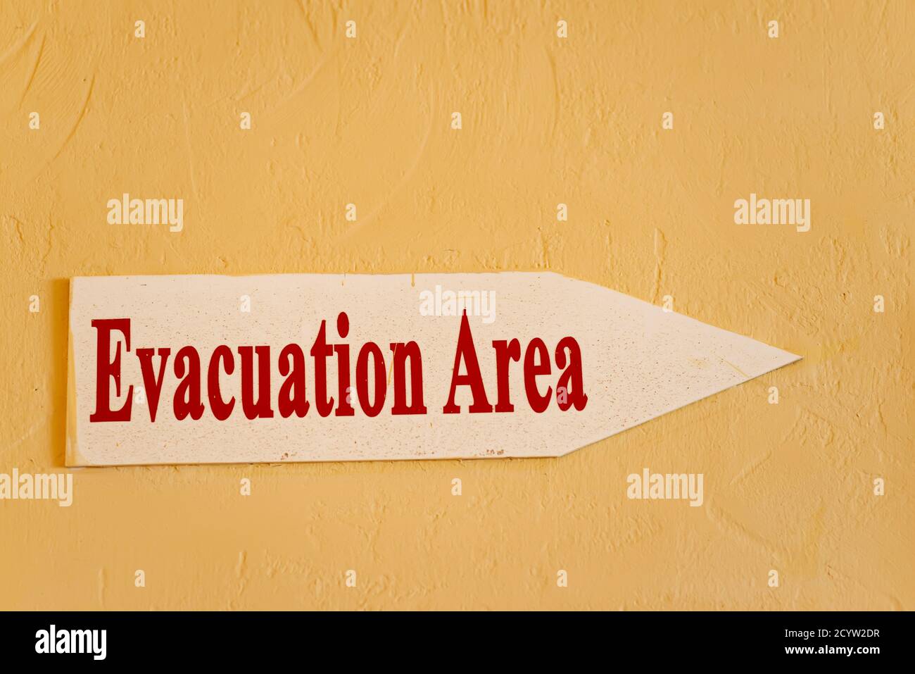Arrow sign with red warning inscription Evacuation Area on a light yellow wall background, copy space. Stock Photo