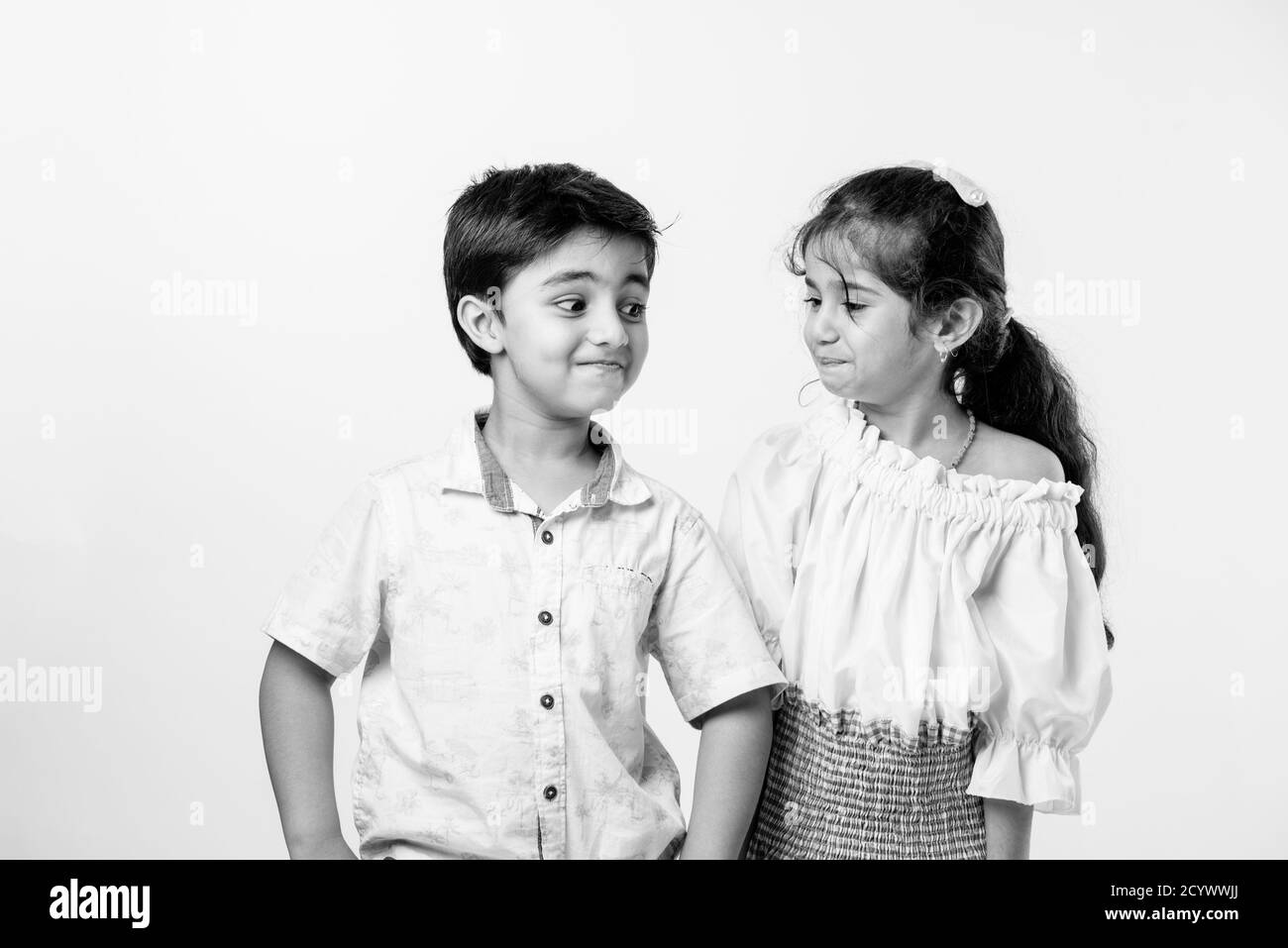 Cute little Indian asian siblings standing and embracing each other in white clothes while standing againstwhite background. Stock Photo