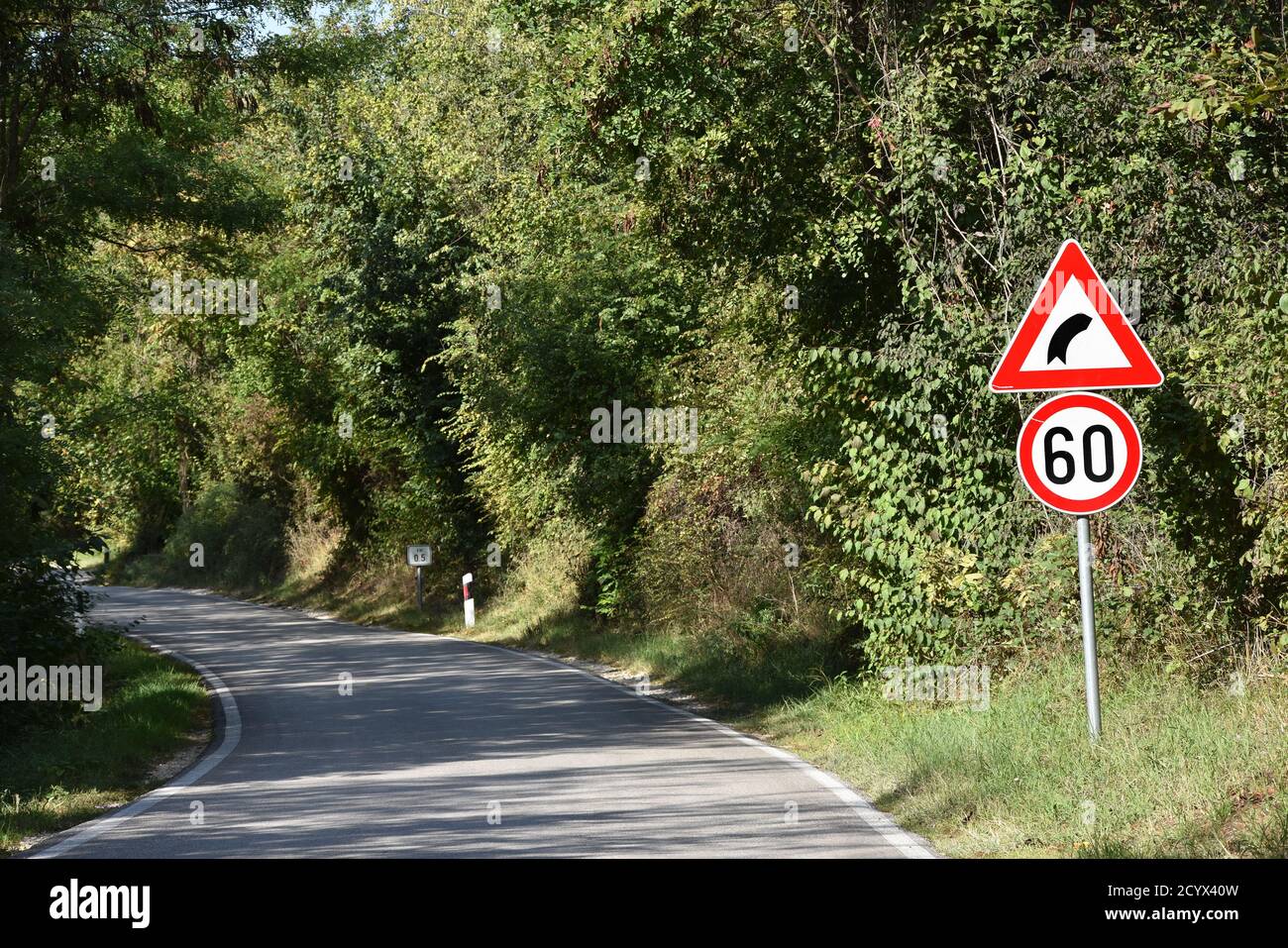 Road signs that shows maximum speed of 60 kilometers per hour and signa that warns drivers on sharp curve on the road ahead Stock Photo