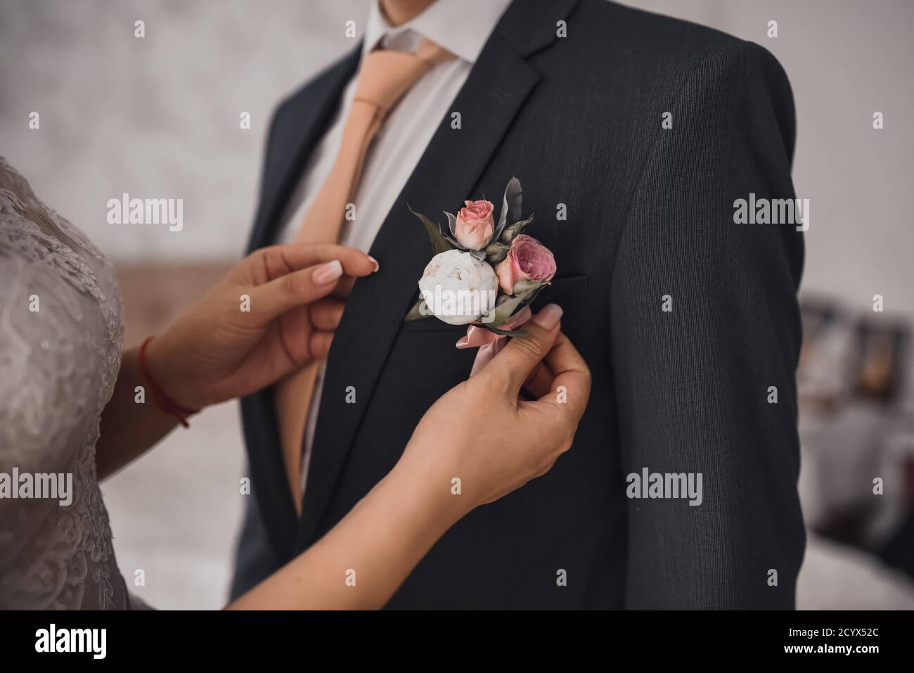bride attaches a boutonniere to a man in black jacket Stock Photo