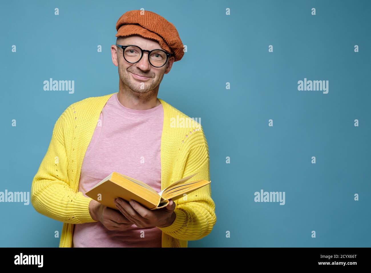 Smiling man in bright clothes, holding an open book in hands and looking at  the camera. Funny creative person. Copy space Stock Photo - Alamy