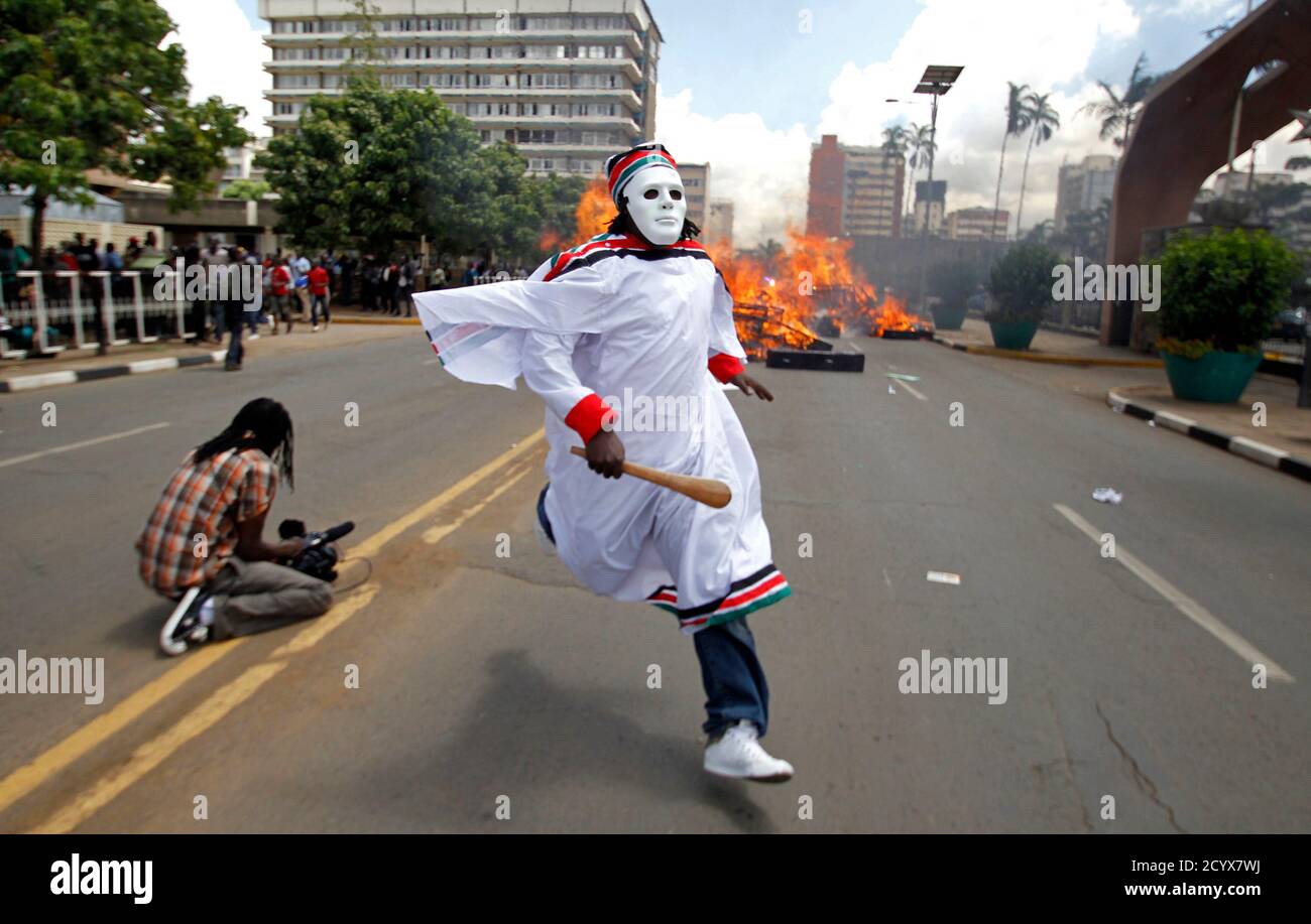 An activist dressed in a religious ceremonial dress runs as mock coffins burn outside the Kenyan parliament during a protest dubbed 'State Burial-Ballot Revolution', a demonstration against legislators plan to receive higher bonuses, in the capital Nairobi January 16, 2013. Kenyans demonstrated in the capital on Wednesday and carried 221 coffins for a mock state funeral of Kenyan legislators protesting over a move by members of parliament to triple their end of term bonuses and award themselves diplomatic passports, bodyguards for life and state funeral, which Kenya's president rejected. REUTE Stock Photo