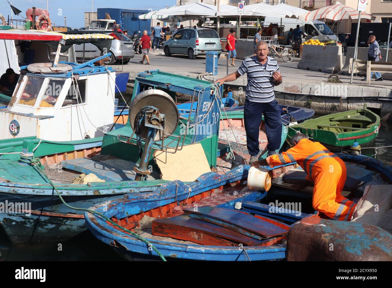 Fisherman cleaning the decks of his boat and chatting to fisherman friend in the harbor in Trapani Old Town Sicily Stock Photo
