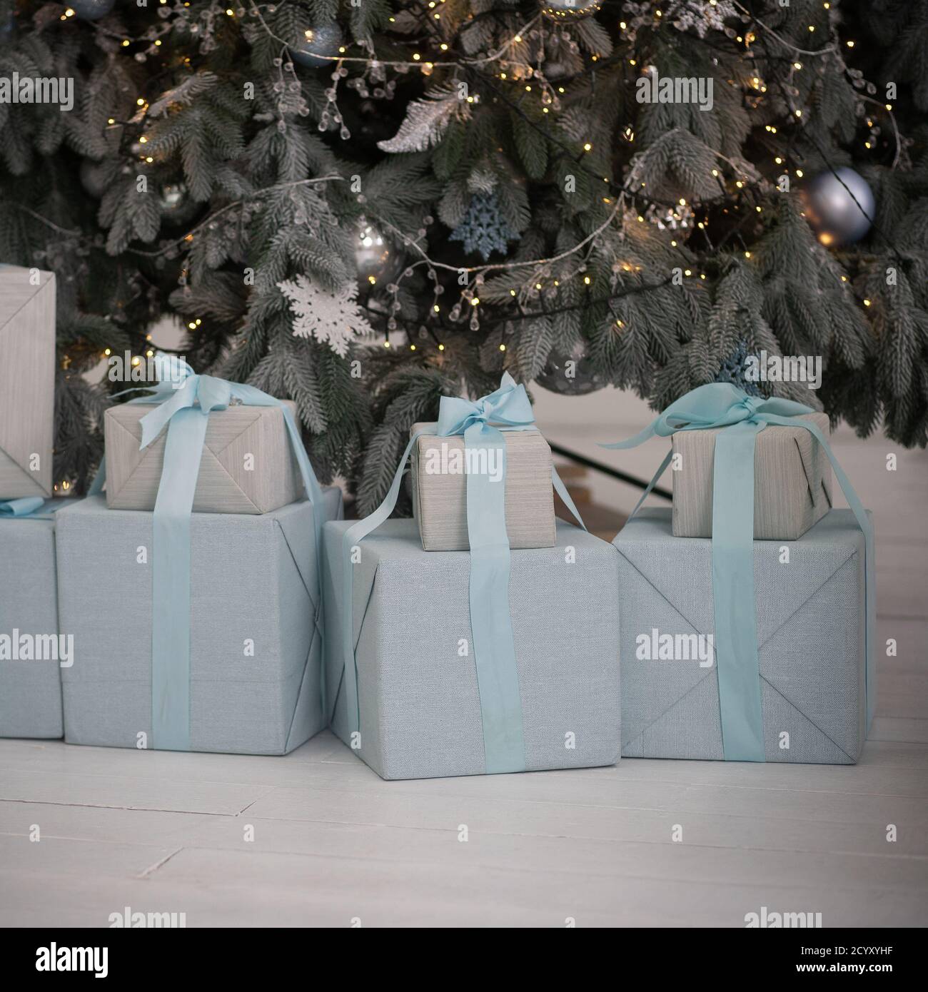Christmas presents in blue wrappers with blue ribbons stand under the Christmas tree. Christmas tree branches are decorated with garlands. High Stock Photo