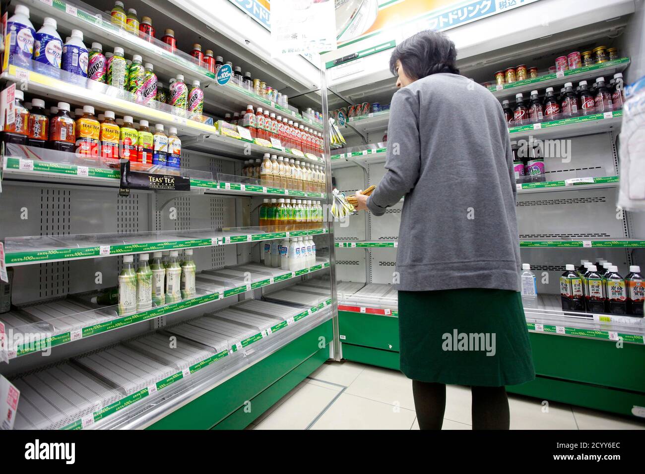 A woman stands near shelves of bottled drinks that are running out at a convenience store in central Tokyo March 24, 2011. Many shops in Tokyo ran out of bottled water on Thursday after radiation from a damaged nuclear plant made tap water unsafe for babies, while more countries imposed curbs on imports of Japanese food. Engineers are trying to stabilise the Fukushima nuclear facility nearly two weeks after an earthquake and tsunami battered the complex and devastated northeast Japan.   REUTERS/Aly Song (JAPAN - Tags: DISASTER FOOD SOCIETY) Stock Photo