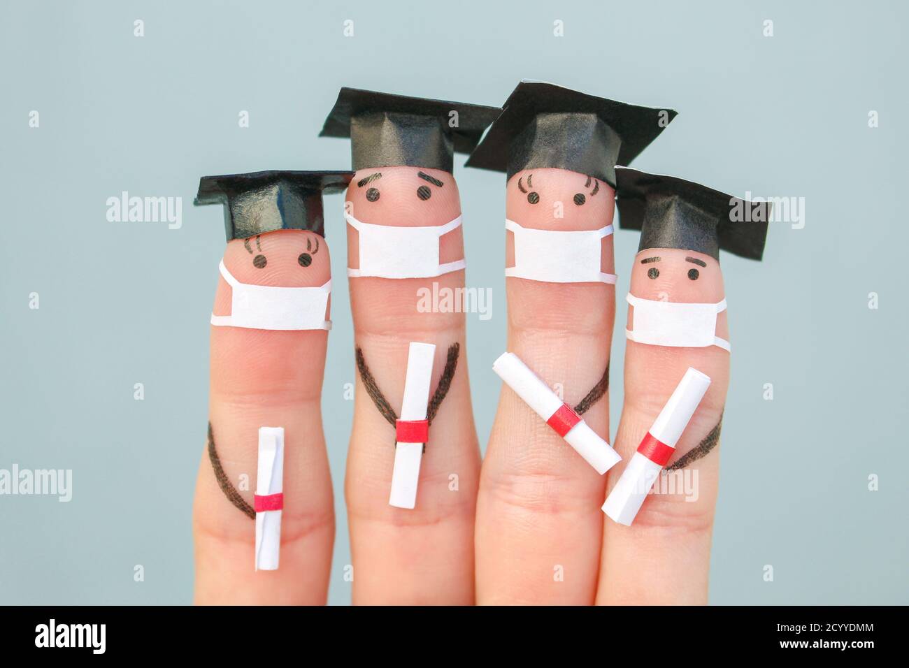Fingers art of students in medical mask from COVID-2019. Graduates holding their diploma after graduation. Stock Photo