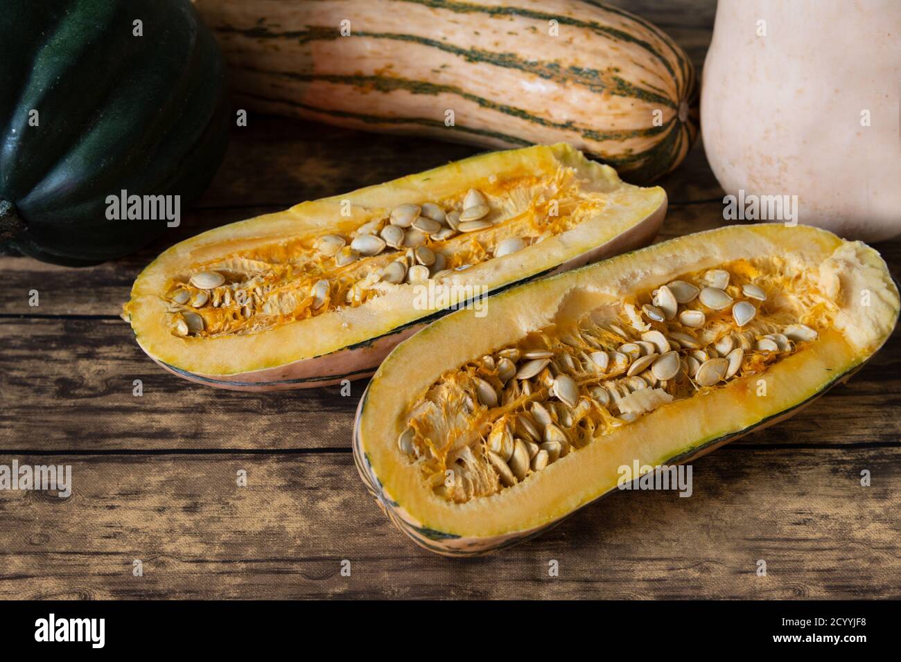Three types of winter squash, Delicata Squash, acorn squash and butternut squash, the delicata squash is cut in half, viewed from an angle, on wooden Stock Photo