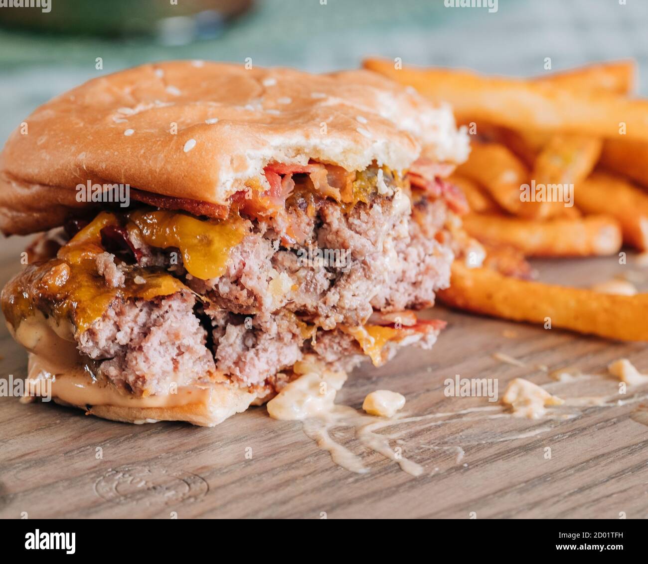 Half eaten bacon cheeseburger with french fries on wooden plate Stock Photo