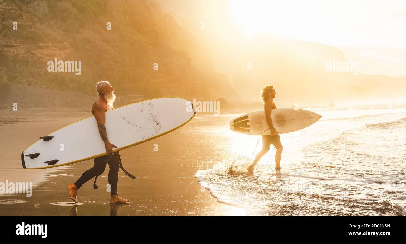Happy friends with different age surfing together on tropical ocean - Sporty people having fun during vacation surf day Stock Photo