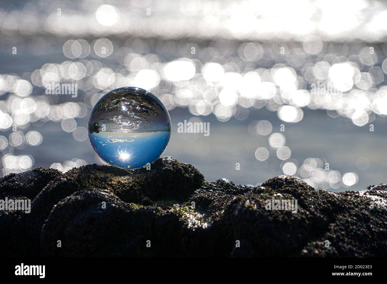 Photography Crystal Photo Ball showing upside down reflection of sky beach and waves balanced on rocks on sandy beach. Stock Photo
