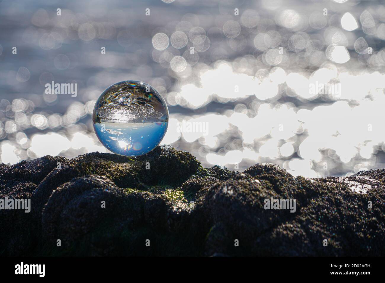 Photography Crystal Photo Ball showing upside down reflection of sky beach and waves balanced on rocks on sandy beach. Stock Photo