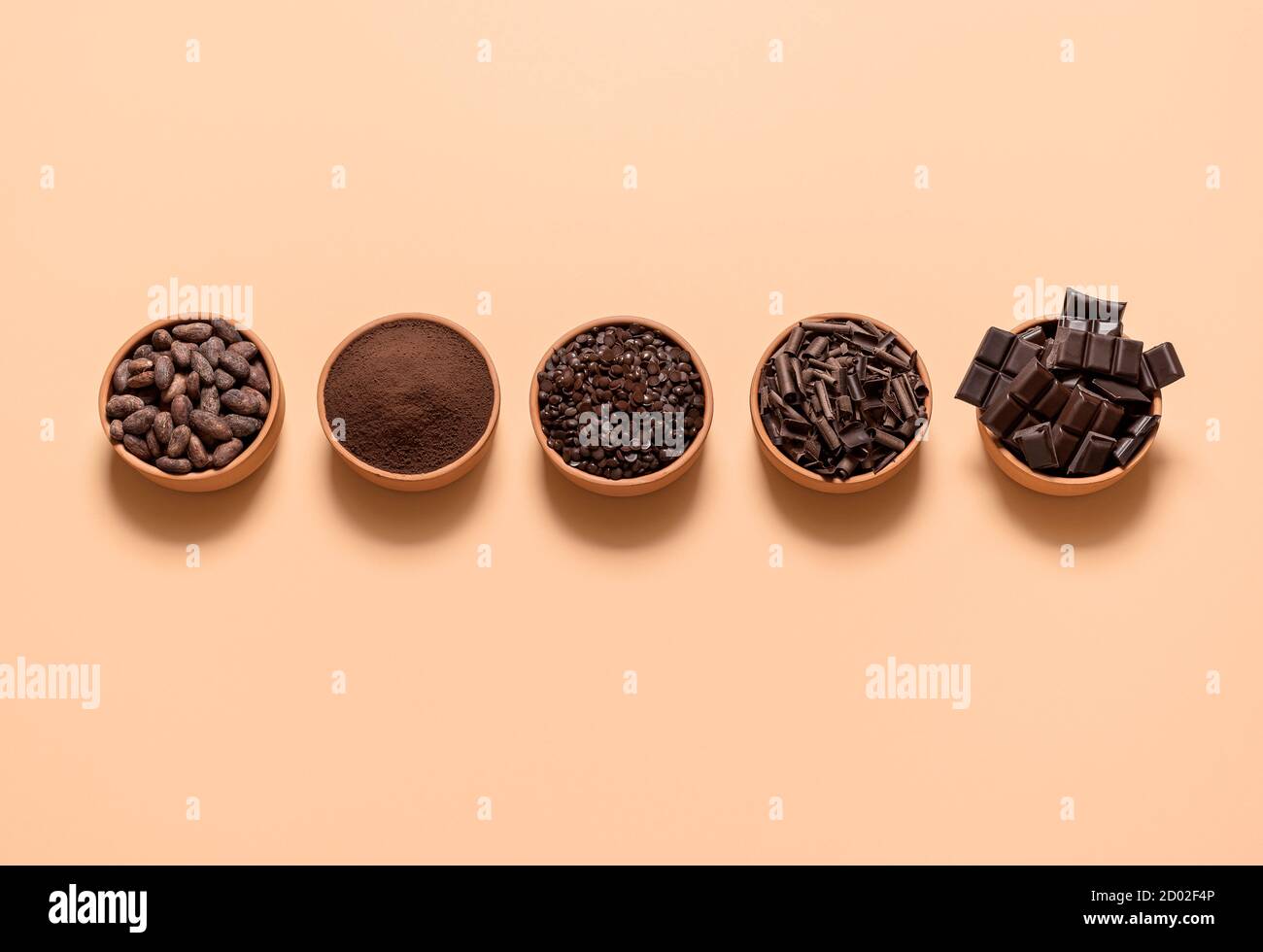 Chocolate ingredients, cacao beans, cocoa powder, chocolate chunks in bowls, isolated on a beige background. Flat lay with cocoa and dark chocolate. Stock Photo