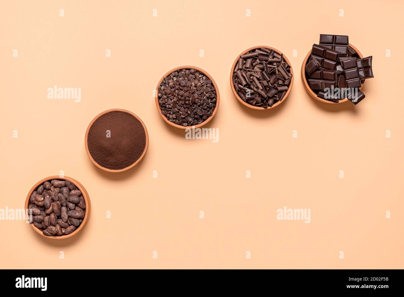 Organic cacao beans and chocolate chunks in ceramic bowls, isolated on a beige background. Flat lay with chocolate ingredients and cocoa powder. Stock Photo