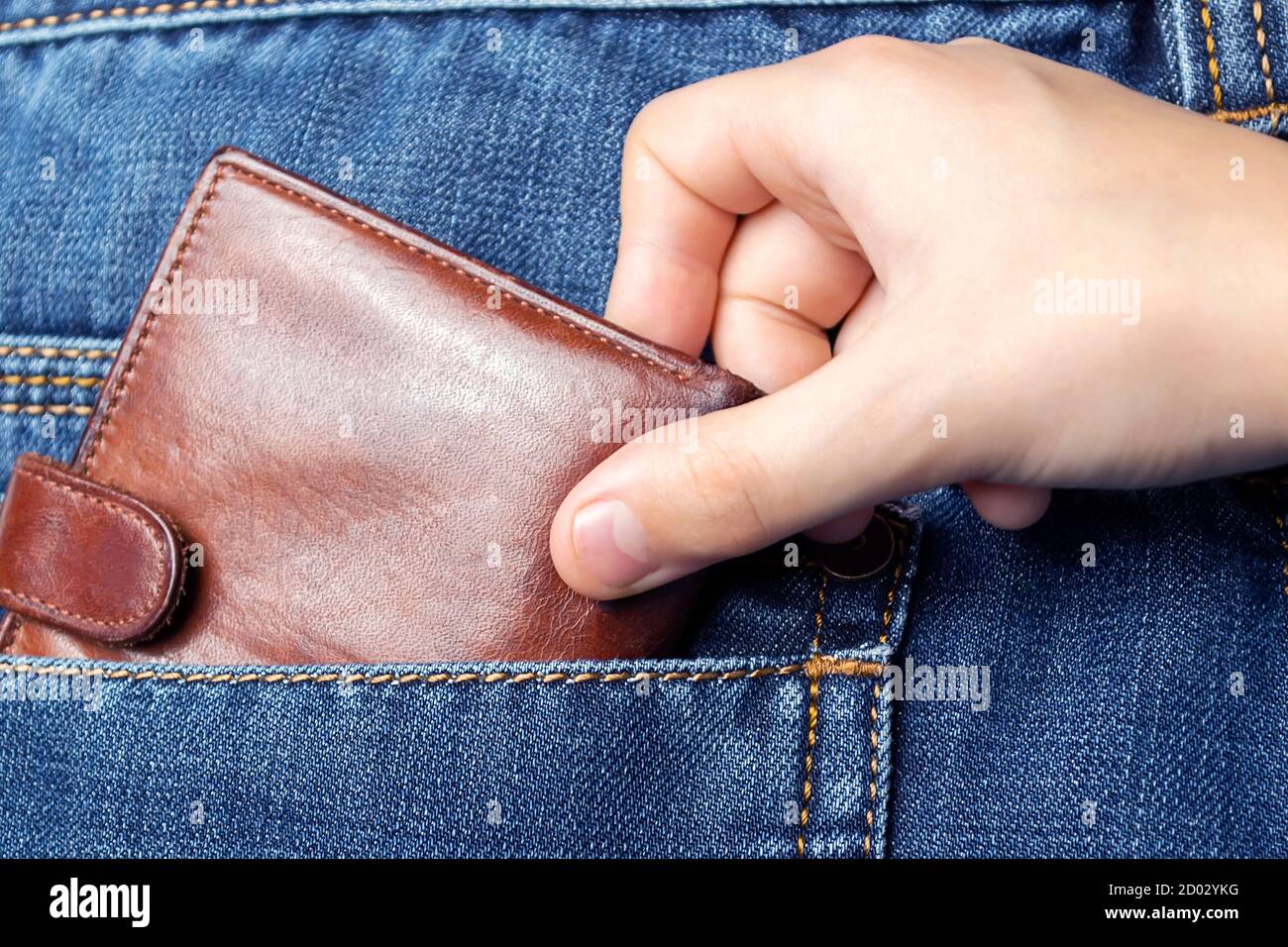 A hand pulls a wallet out of the back pocket of his jeans.The concept of pickpocketing or theft in the family from parents. Stock Photo