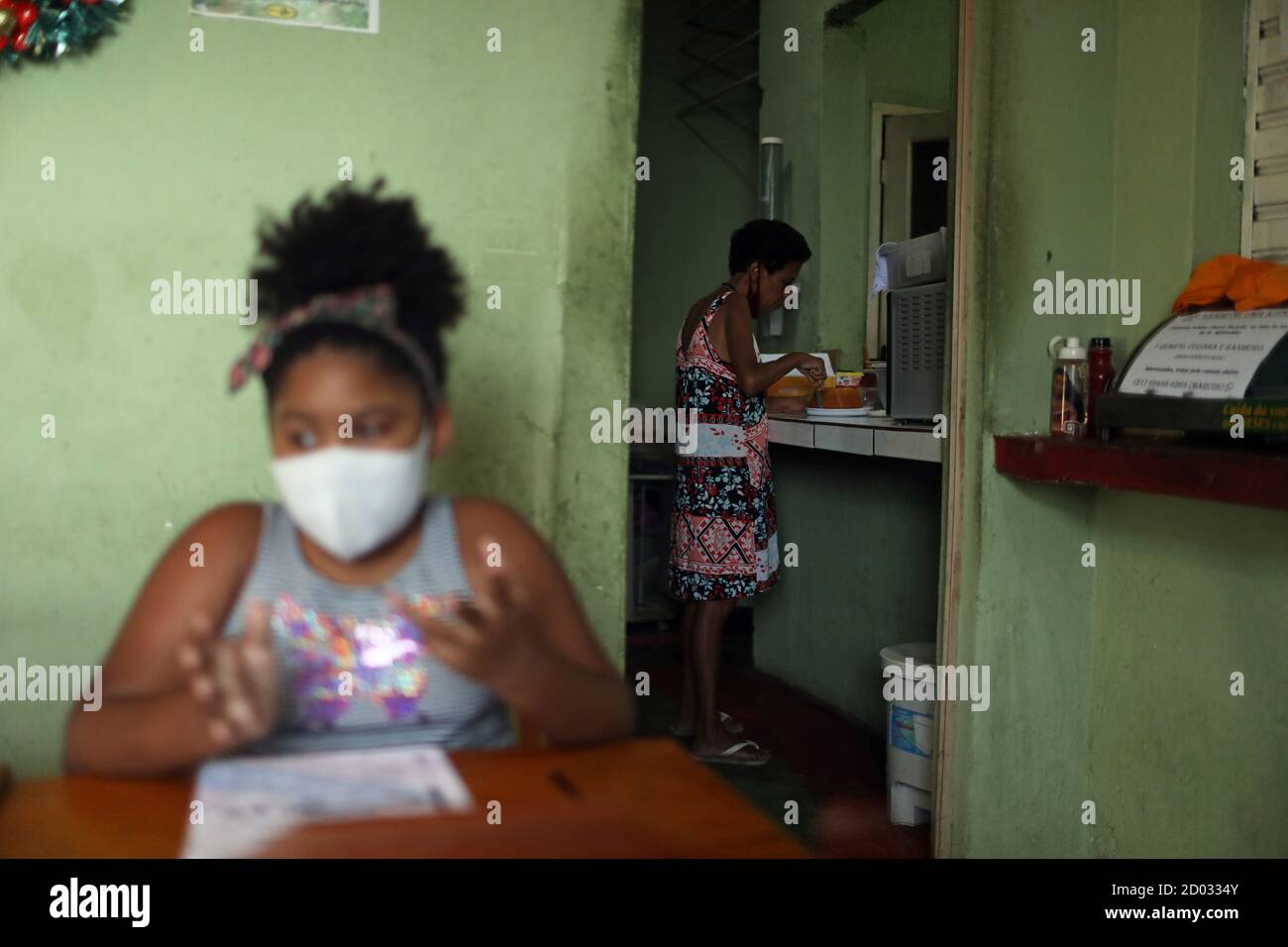 Rebecca Sabino, 8, does her homework as part of the Educacao na Quarentena project (Quarantine Education), as public schools are still closed, while a person waits for food at her family's snack bar at Prazeres slum in Rio de Janeiro, Brazil October 1, 2020. Picture taken October 1, 2020. REUTERS/Pilar Olivares Stock Photo