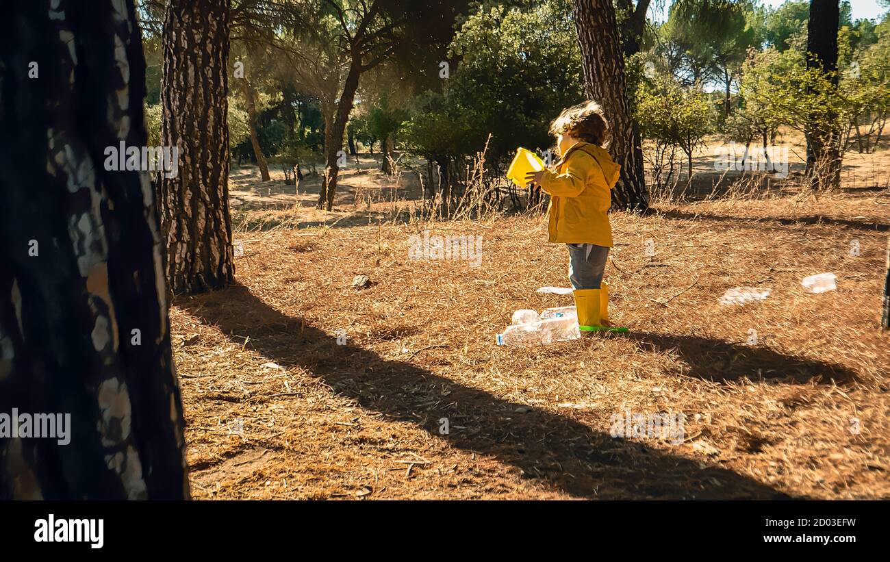 Young child is picking up plastic waste in the forest as a volunteer. Toddler and young children early environmental education concept. Plastic free Stock Photo