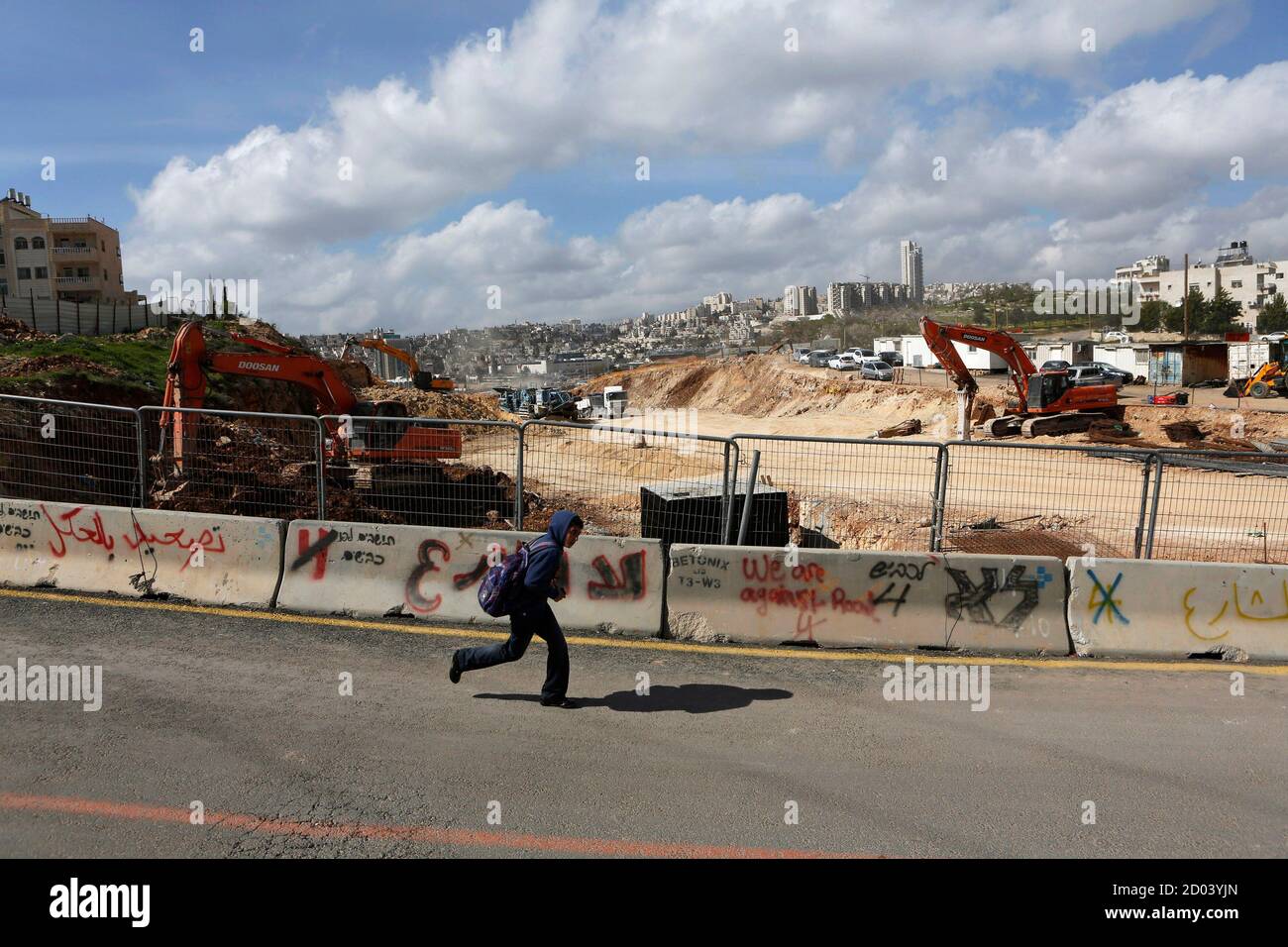 A boy runs past a road under construction in the Arab neighbourhood of Beit Safafa in Jerusalem February 28, 2013. The mechanical diggers start work soon after dawn, cutting through a leafy village on the outskirts of Jerusalem to build a six-lane highway that has become the latest focal point of Arab-Israeli discontent. The road leads directly to Jewish settlements, built on occupied land around the foothills of Bethlehem. When finished, it will allow the settlers to speed down to Israel's thriving coastal plains, unhindered by traffic lights or roundabouts. Their gain is coming at the expens Stock Photo