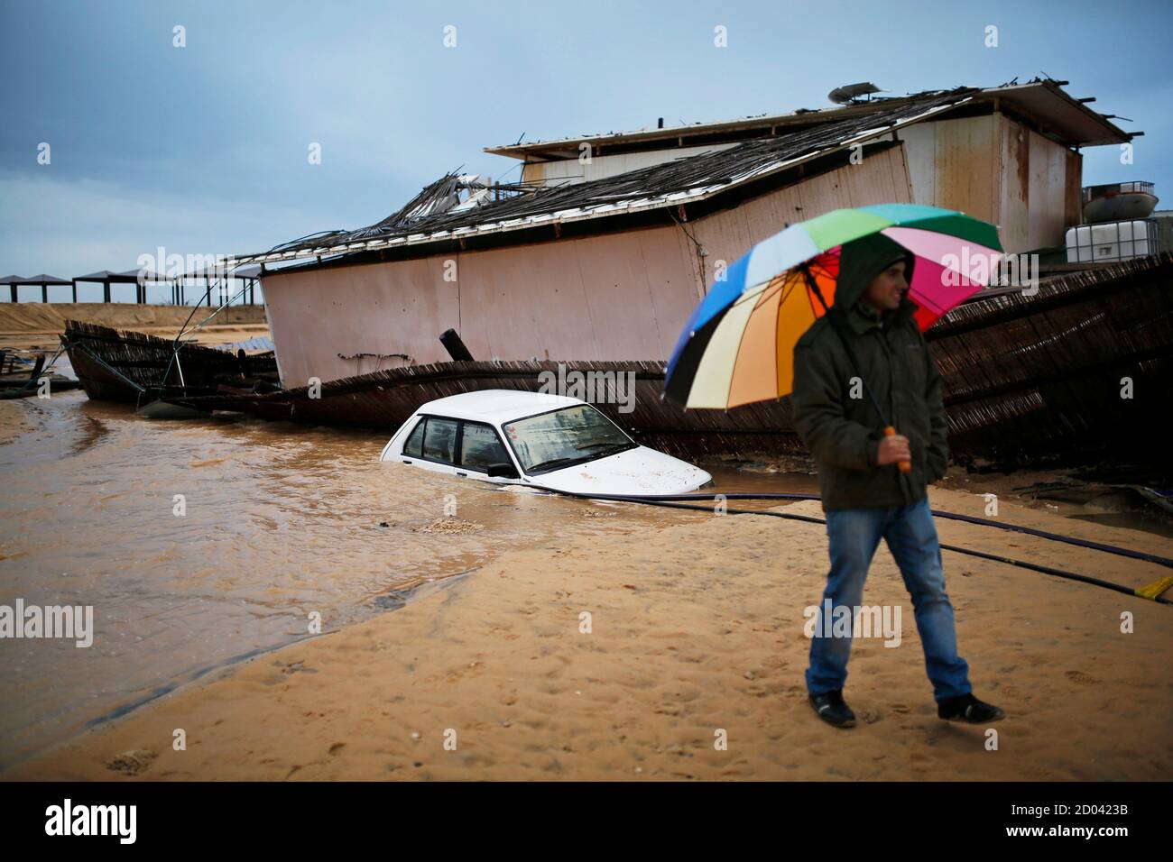 A man walks next to a car and a beach restaurant that sank into the sand following heavy rains and flooding on a beach of the Mediterranean sea near Kibbutz Nitzanim in southern Israel December 14, 2013. REUTERS/Amir Cohen (ISRAEL - Tags: ENVIRONMENT TPX IMAGES OF THE DAY) Stock Photo