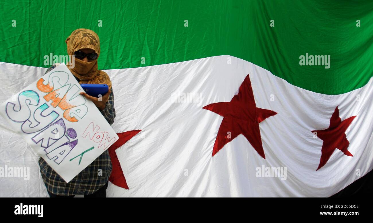 A Syrian Living In Malaysia Holds A Placard As She Attends To Her Text Messages In Front Of A Giant Syrian Independence Flag During A Protest Against President Bashar Al Assad Outside The
