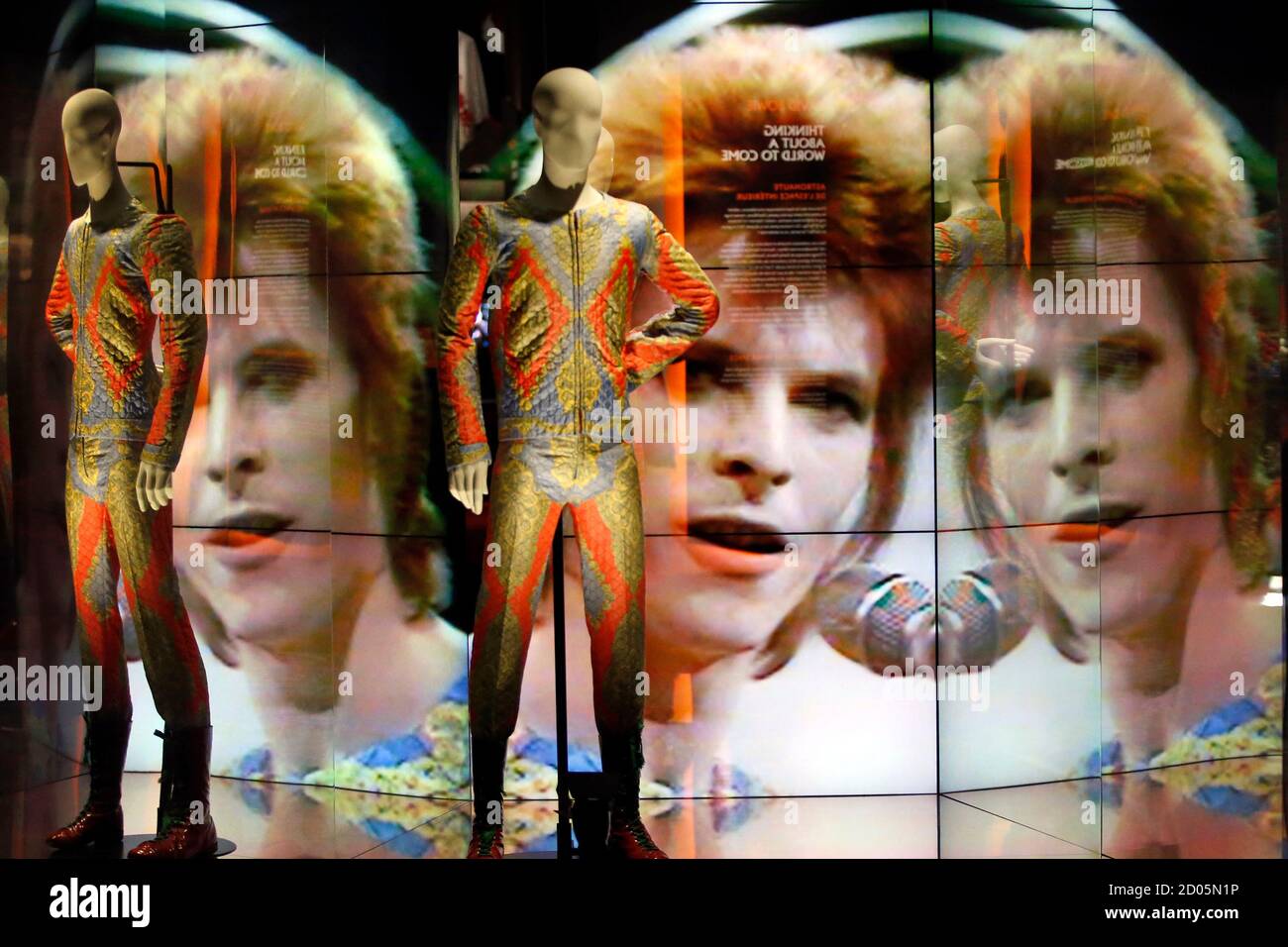 Two suits designed by Freddie Burretti (1972) for the Ziggy Stardust tour  are displayed in front of a video showing pop star David Bowie singing at  the BBC show Top of the