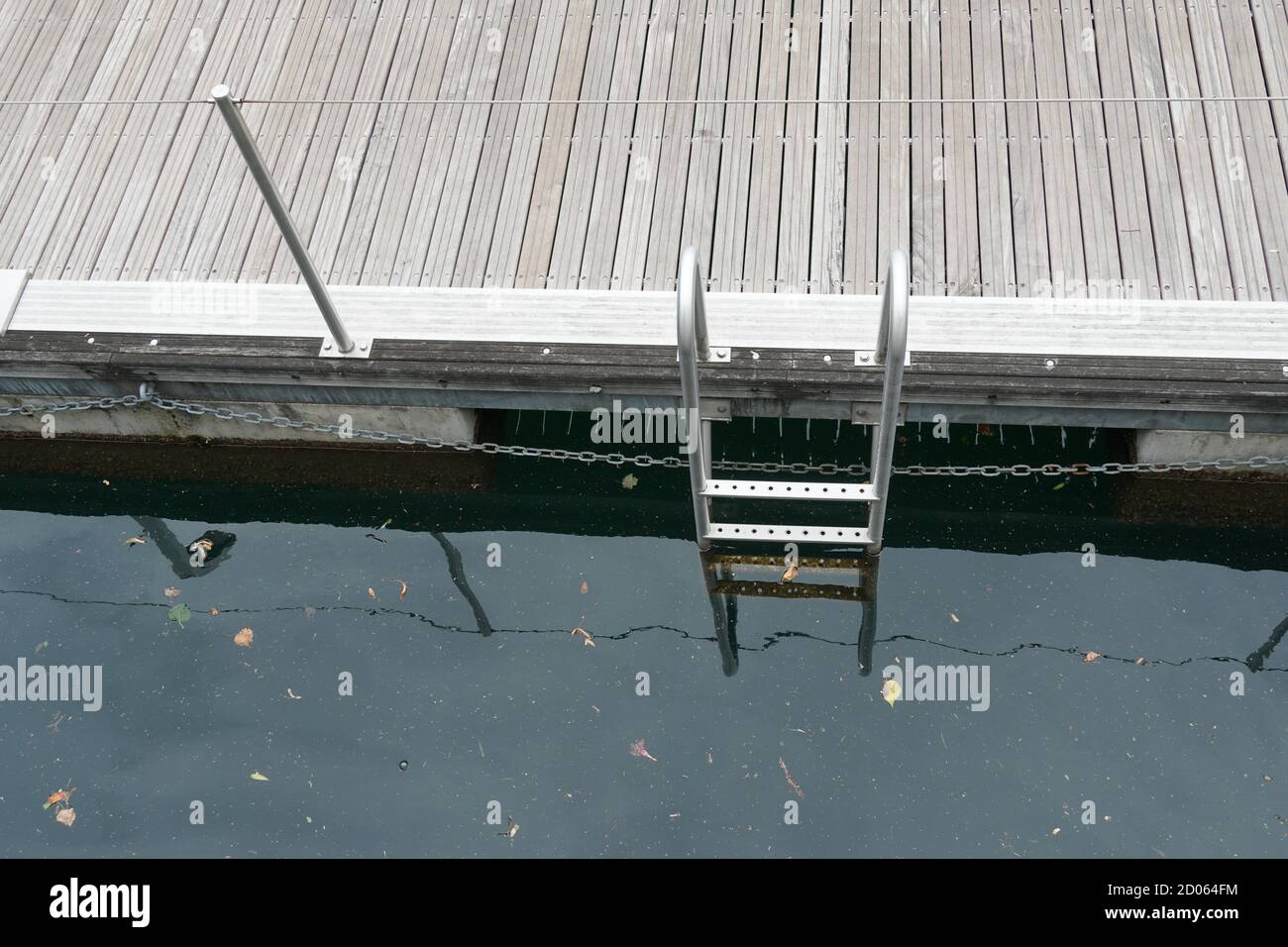 Metal ladder for descending into the water in marina in Locarno, Switzerland. The ladder reflects in the water and the reflection makes it seem longer Stock Photo