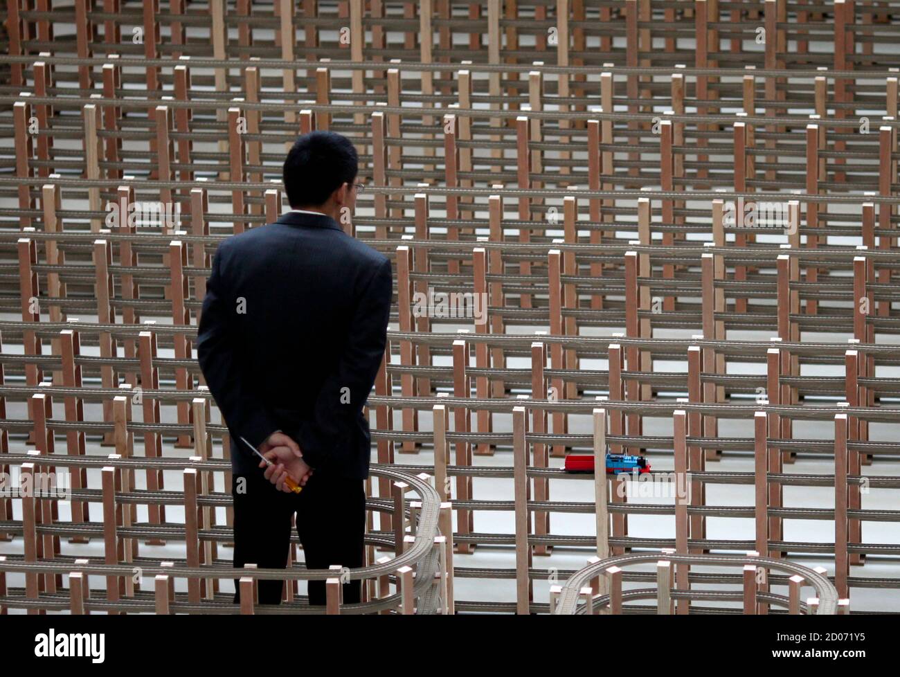 A staff member watches as a toy train travels along the 2.888-kilometer plastic track during an event organized by toy manufacturer Mattel to set a Guinness World Record in Shanghai November 24, 2012. Thomas & Friends, a brand belonging to the world's largest toy manufacturer Mattel, set the new record for the World's Longest Plastic Toy Train Track. The track was composed of 13,769 individual sections of plastic toy train track, forming a total of seven layers of track. The new world-record-winning track covers approximately 200 square meters, and the total length of the track measures six ti Stock Photo