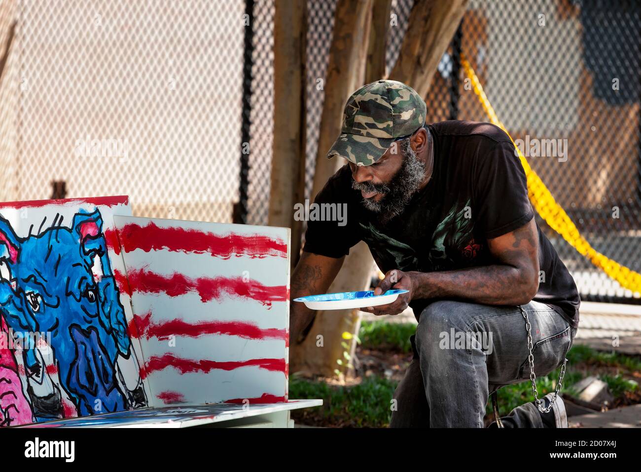 An artist paints a piece of protest art depicting police as pigs against a background with an American flag motif, Washington, DC, United States Stock Photo