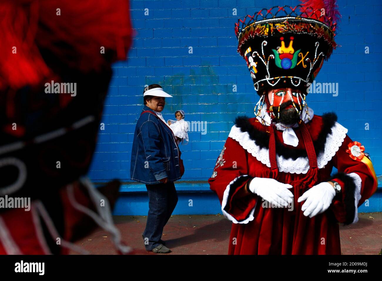 A Chinelo (R) costumed dancer stands nearby as a woman walks past with a  dressed-up doll representing the baby Jesus, during a celebration to mark  40 days after the birth of Jesus,