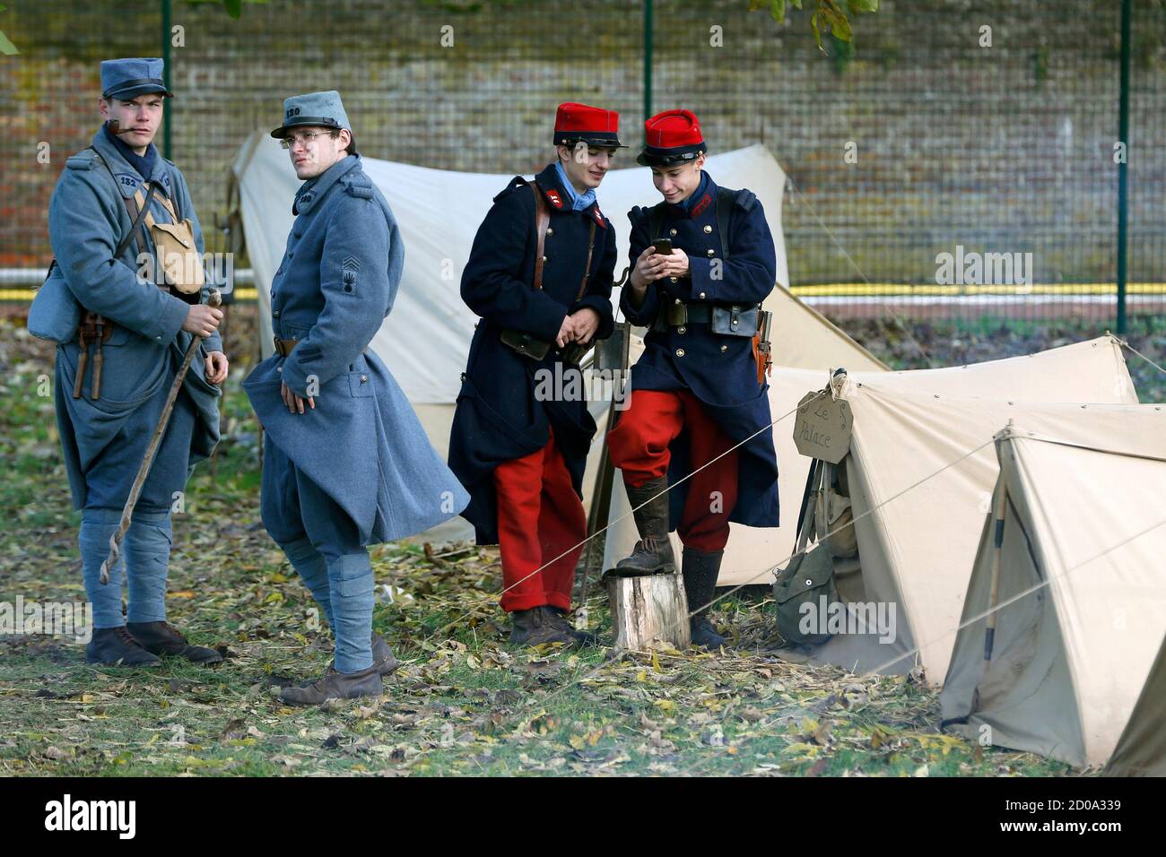 Thomas and Brice (R) check a mobile phone next to Guillaume (L) and Andy, dressed with vintage army uniforms as Poilu (French soldier in World War I) at a bivouac camp of World War One Historical Association '14-18 en Somme' in Fouilloy, Northern France, November 10, 2013. The historical association '14-18 en Somme' was created in August 2009 by French history teacher Sylvain Pinard with the aim of keeping alive the memory of the soldiers of World War One, and promoting understanding of the battles of the Great War. Armed with their motto 'Never forget, always remember', the 30 members live, e Stock Photo