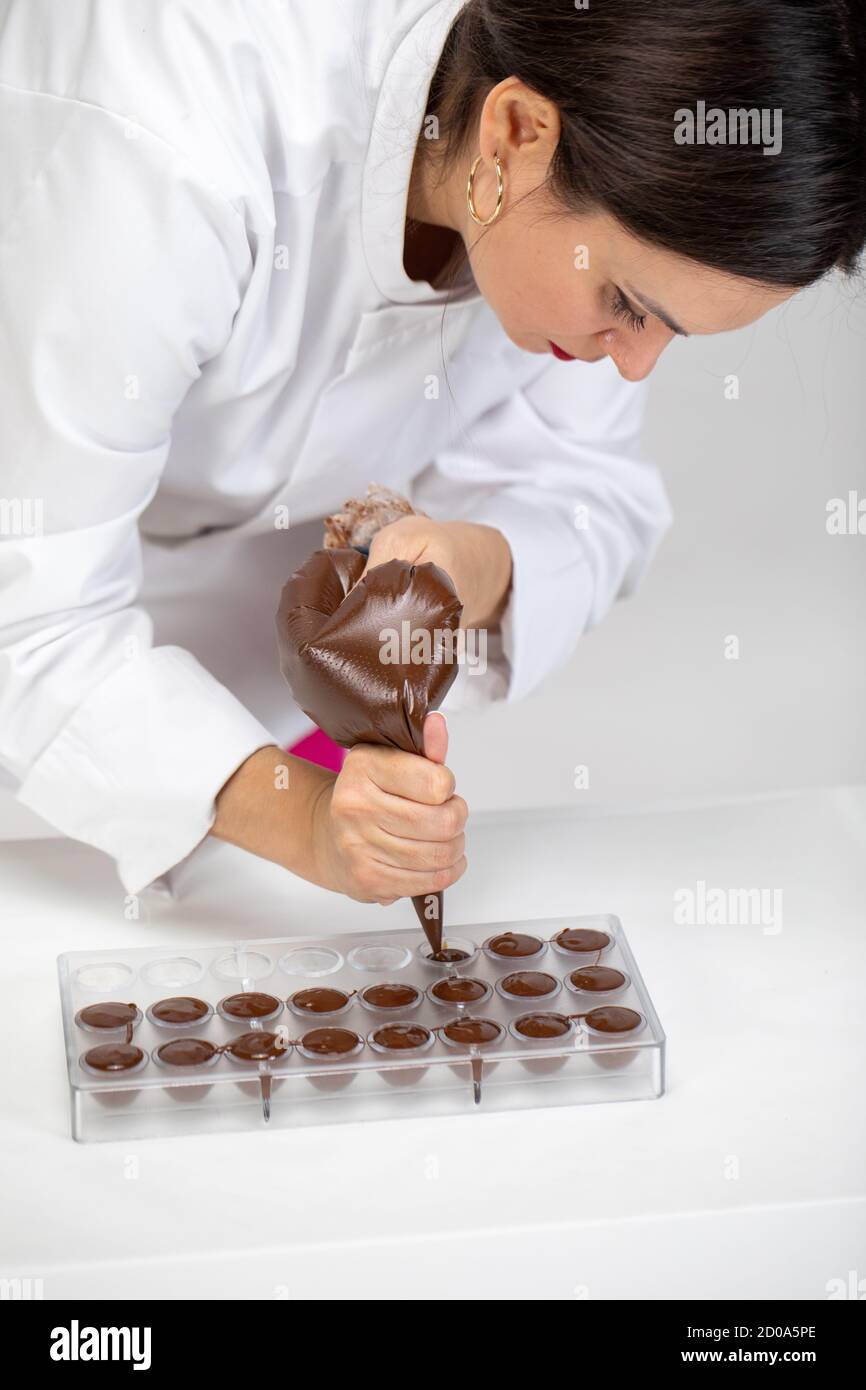 Chef pouring dark melted chocolate into mold with pastry bag, hand