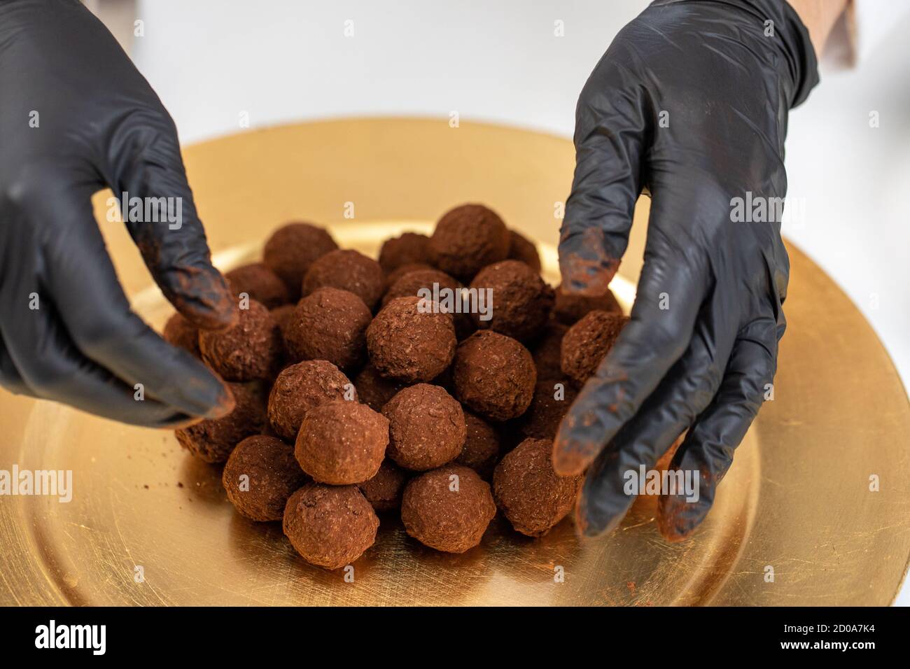 Closeup chef puts pile of dark chocolate truffles in gold dust on golden plate Stock Photo