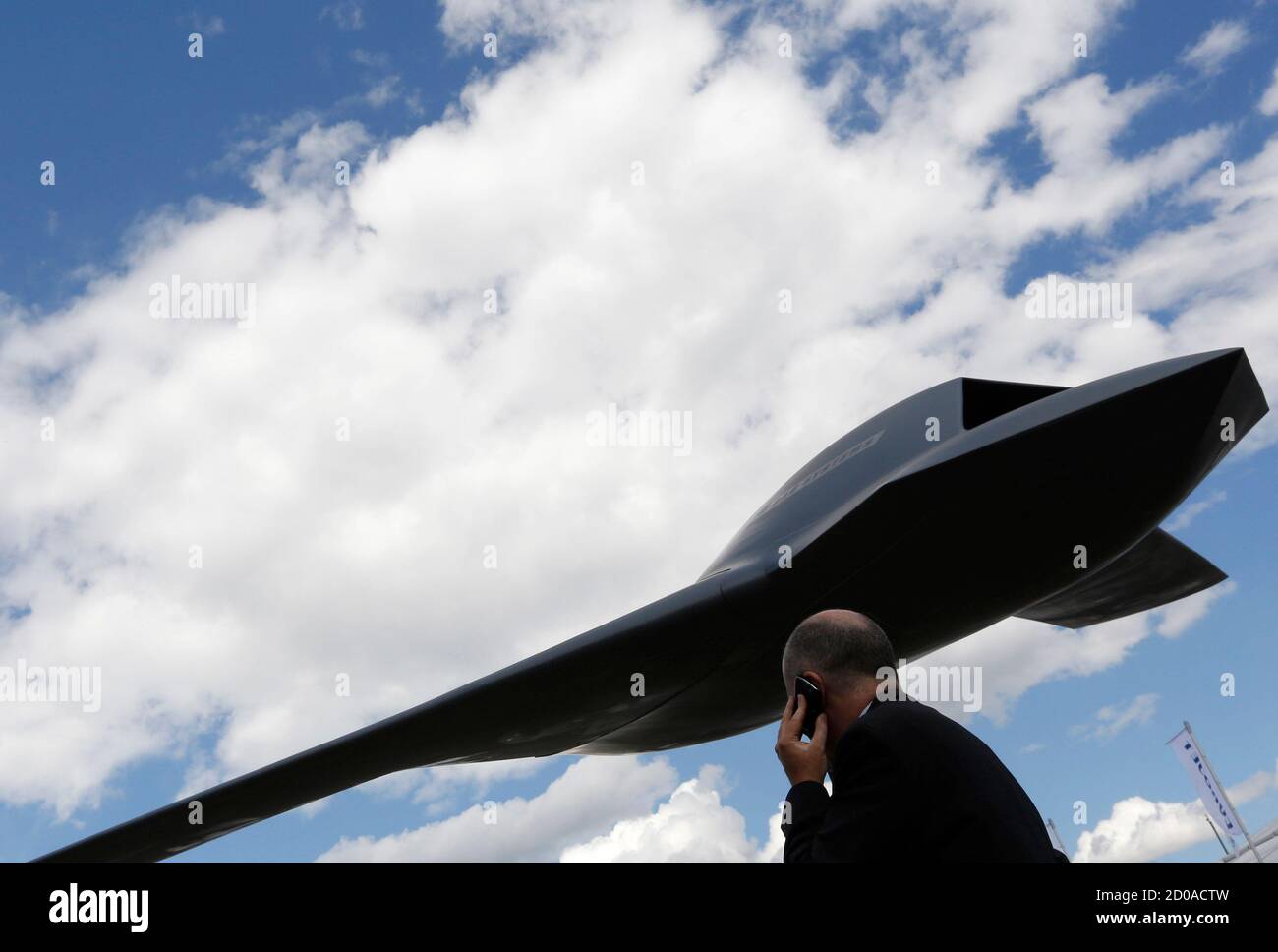 A man speaks on his phone next to a BAE Systems potential concept model of an unmanned combat system, also known as a drone, at the Farnborough Airshow in southern England July 11, 2012.  REUTERS/Luke MacGregor  (BRITAIN - Tags: TRANSPORT BUSINESS MILITARY) Stock Photo