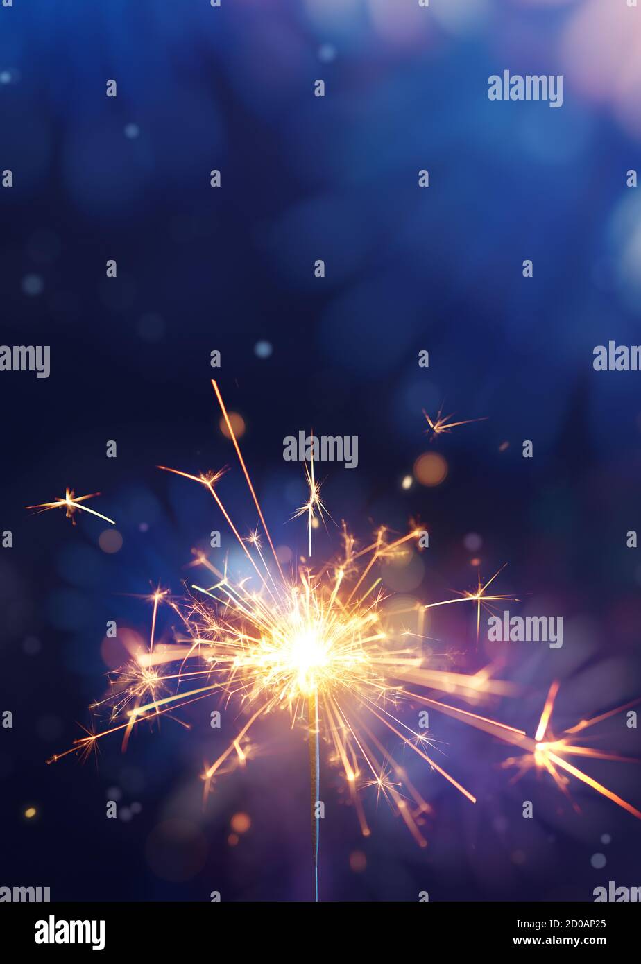 Glittering burning sparkler against fireworks background with copy space Stock Photo