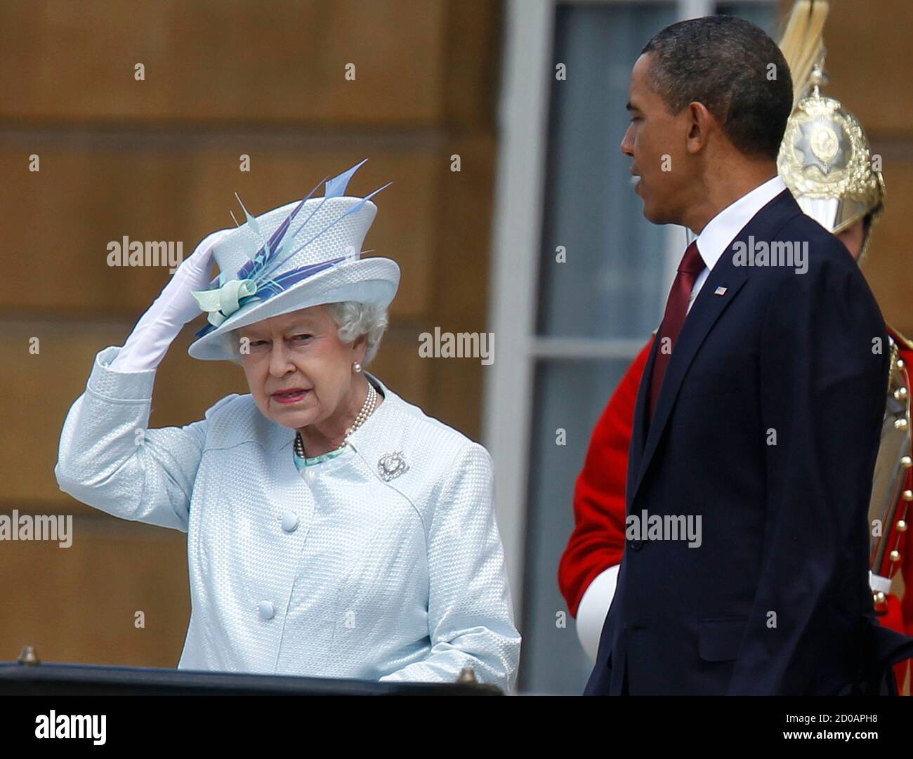 U.S. President Barack Obama looks on as Britain's Queen Elizabeth II holds on her hat as the wind blows during an official arrival ceremony on the Buckingham Palace Terrace stairs in London May 24, 2011.         REUTERS/Larry Downing      (BRITAIN - Tags: POLITICS ROYALS) Stock Photo