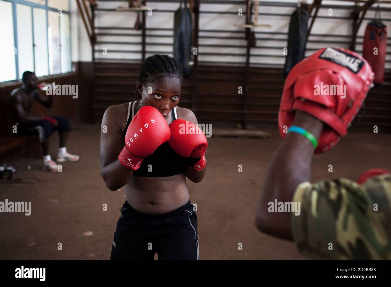 Olympic hopeful Zainab Kaite, 21, holds her guard while working out with her trainer at the national stadium in Sierra Leone's capital Freetown, April 25, 2012. Sierra Leone's national boxing team was scrambling on Wednesday to raise money to send athletes to an Olympic qualifying event starting in Morocco on Friday, but lack of financing and government support means the competition is likely out of reach for most of the national team. REUTERS/Finbarr O'Reilly (SIERRA LEONE - Tags: SPORT OLYMPICS BOXING) Stock Photo