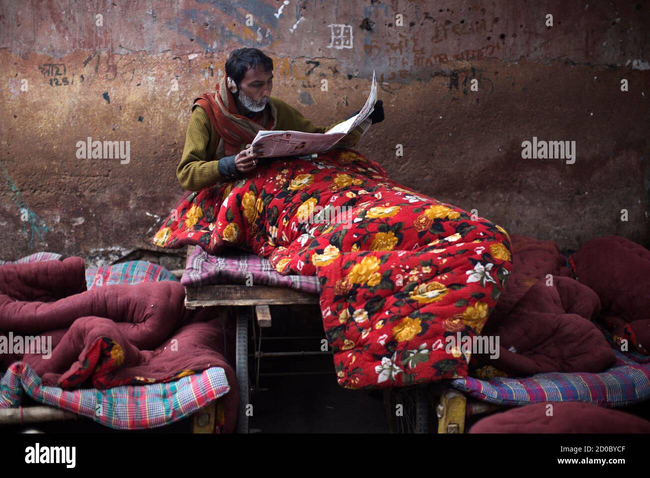 A homeless man reads newspapers as he sits under a quilt at an open space on  a cold winter morning in the old quarters of Delhi January 3, 2013. Heavy  fog and