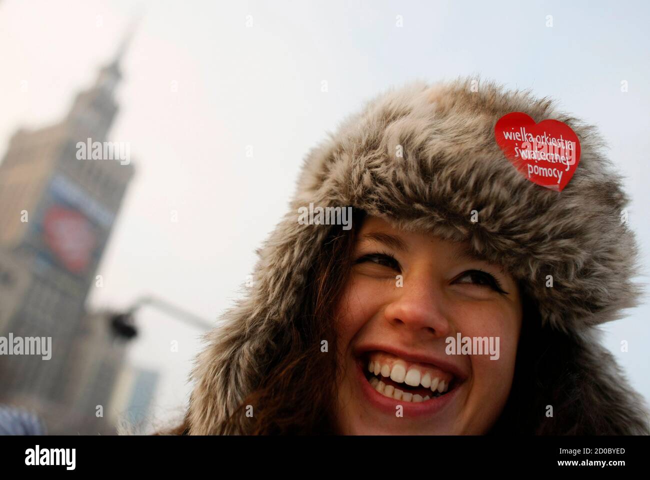 A woman smiles as she wears a sticker with a sign of the Christmas Charity  Foundation (Wielka Orkiestra Swiatecznej Pomocy) on her hat during an  annual charity event in front of the