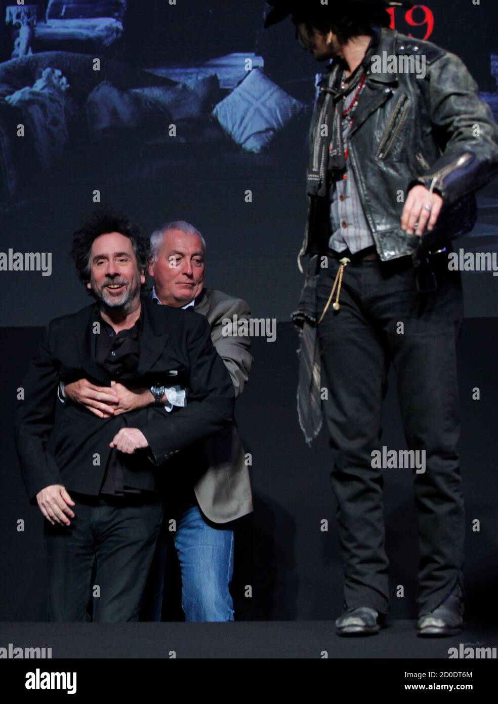 A member of staff grasps director Tim Burton (L) as actor Johnny Depp looks  on after Burton fell off a stage during a photo call at a news conference  for their film "