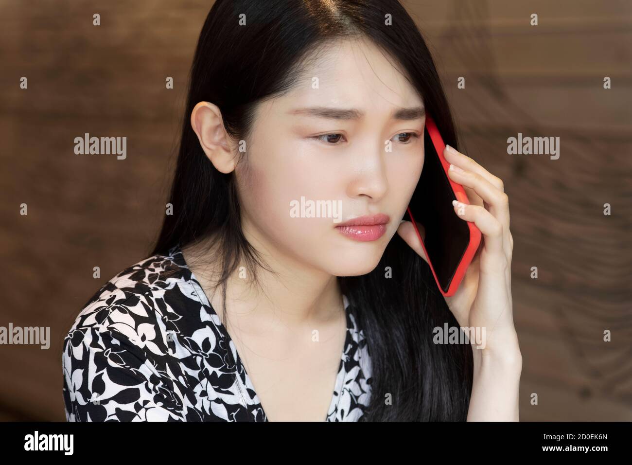 Chinese American woman deep in thought using an red smart phone in a coffee shop Stock Photo